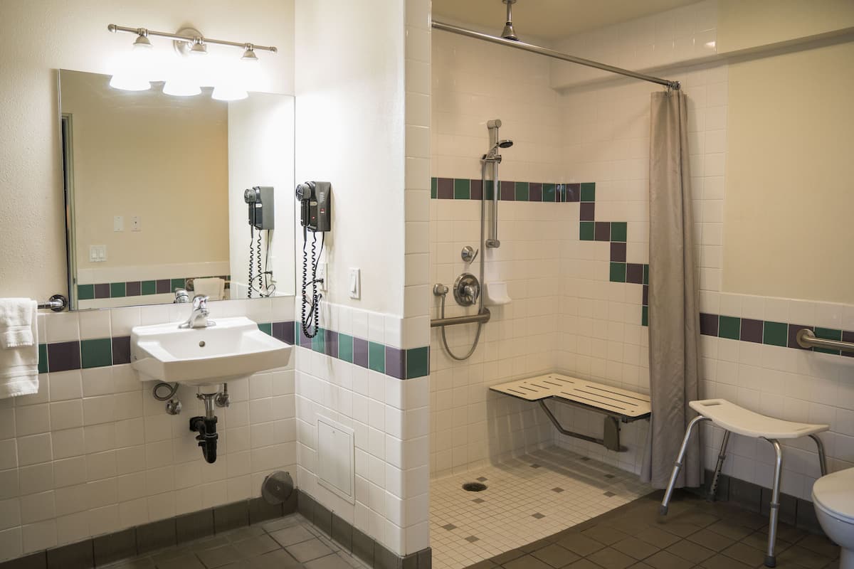 A bathroom with a sink, mirror, hairdryer, shower, bench, and a toilet.