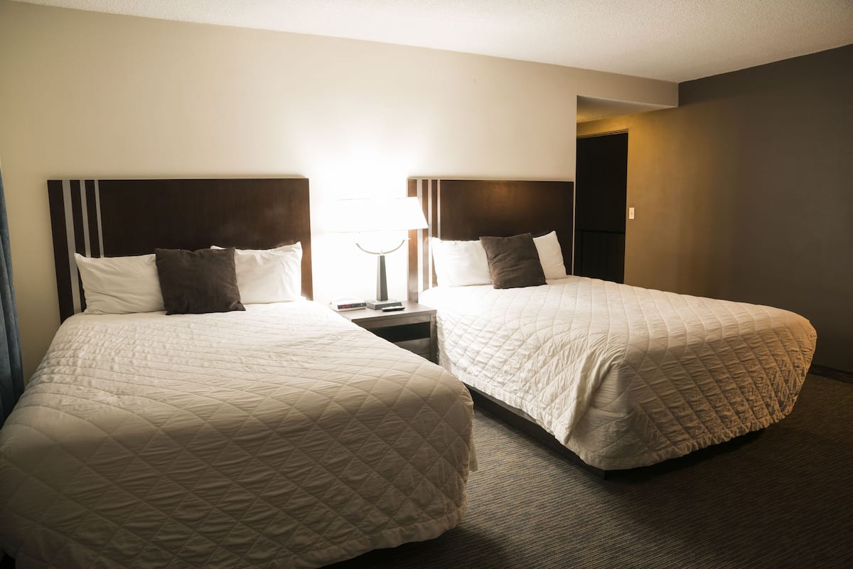 A hotel room with two queen beds, each with a headboard, a nightstand, and a lamp.