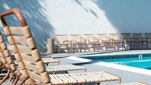 Un espace aménagé au bord de la piscine, avec des chaises longues et une petite table, un bac à fleurs en pierre et une piscine dont le bord est revêtu de carreaux.