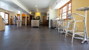 Un hall d’hôtel spacieux comprenant un comptoir d’accueil, un guichet et un espace détente avec des chaises et des tables en métal.