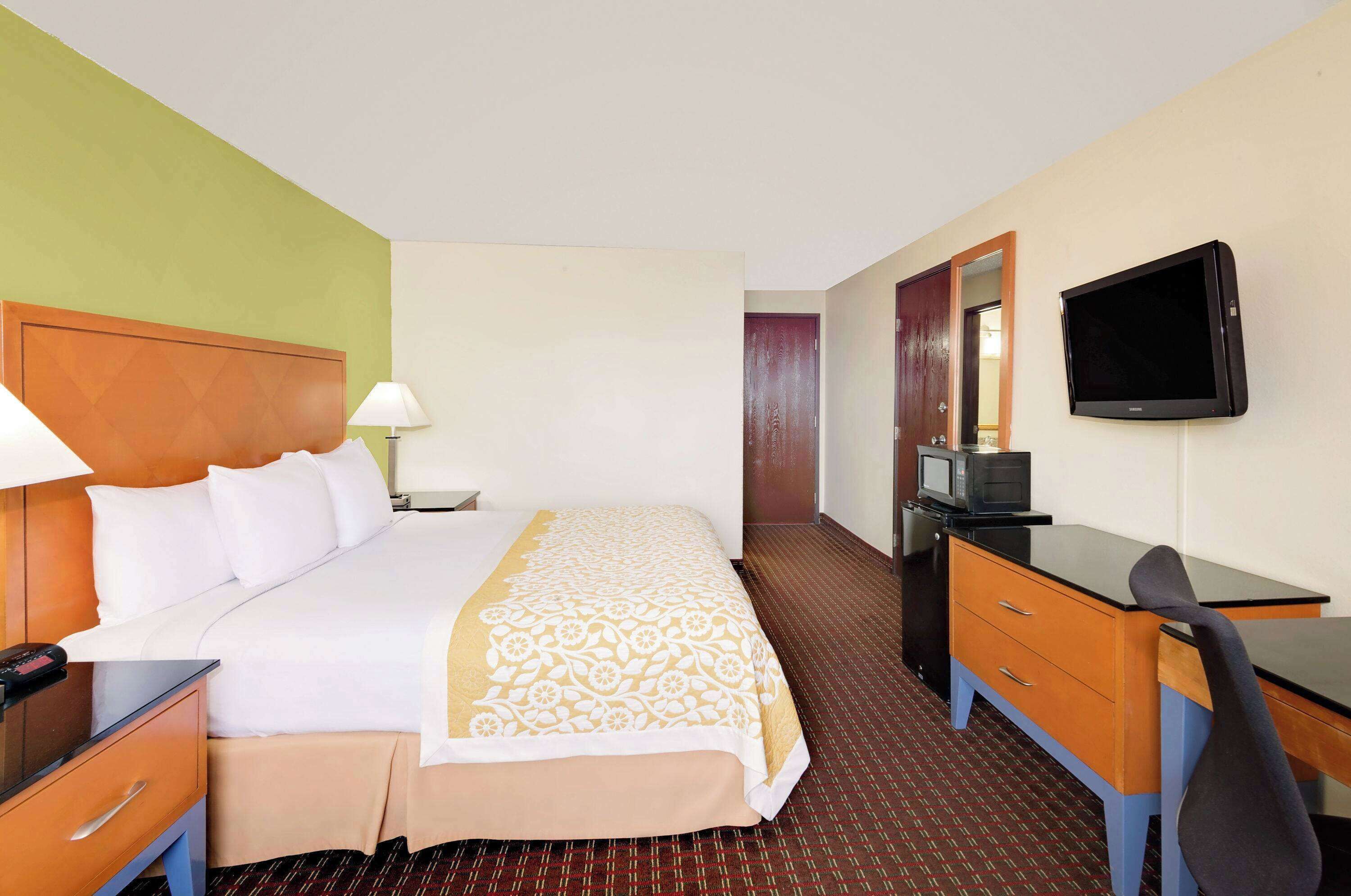 Een hotelkamer met een bed, bureau, stoel, televisie en een spiegel.