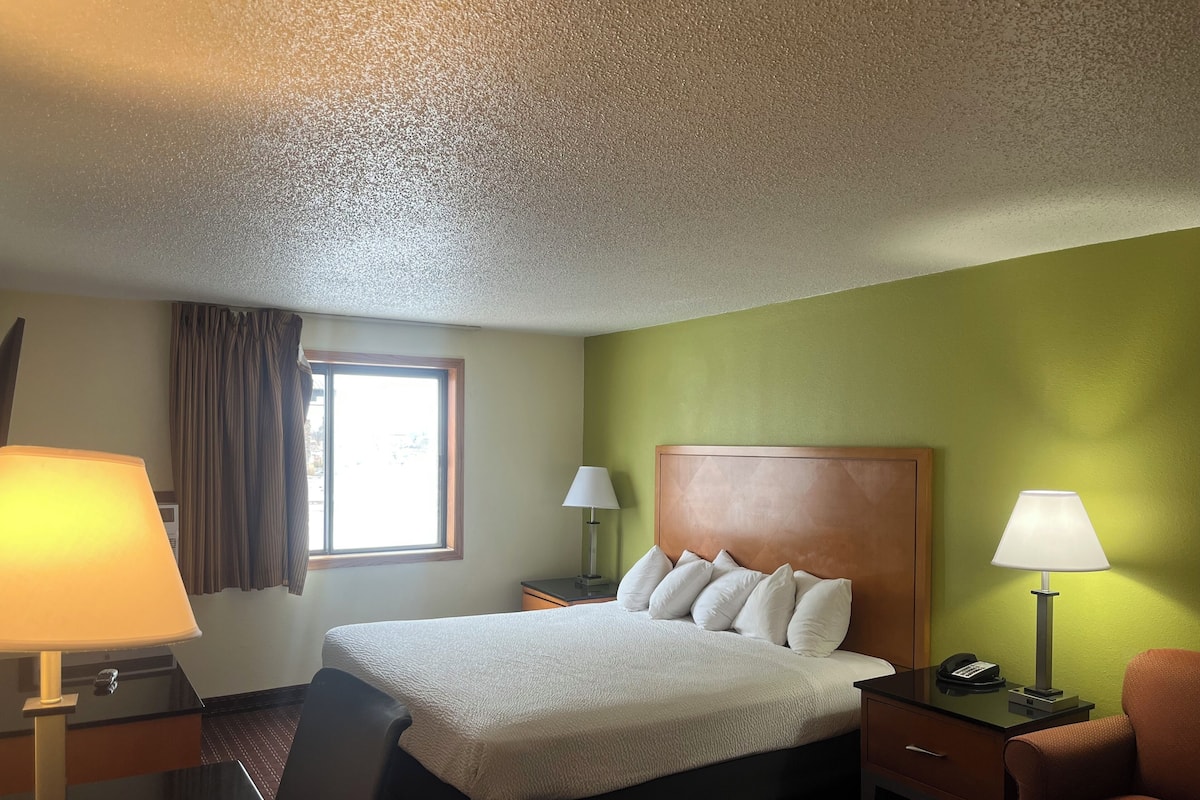 A hotel room with a bed, two bedside tables, a chair, a window with curtains, and a lamp on each table.