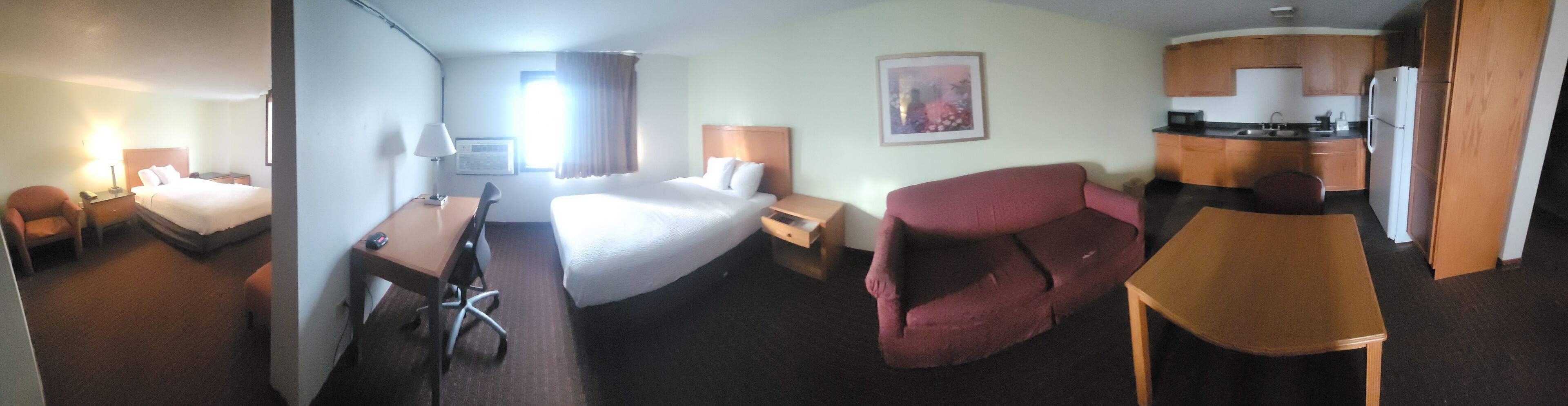 A hotel room with a bed, desk, chair, and kitchenette.