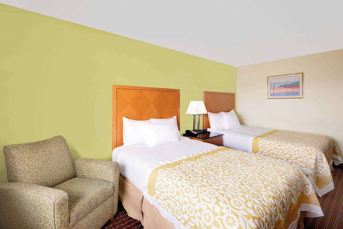 A hotel room with two beds, a sofa, a nightstand, and a painting on the wall.