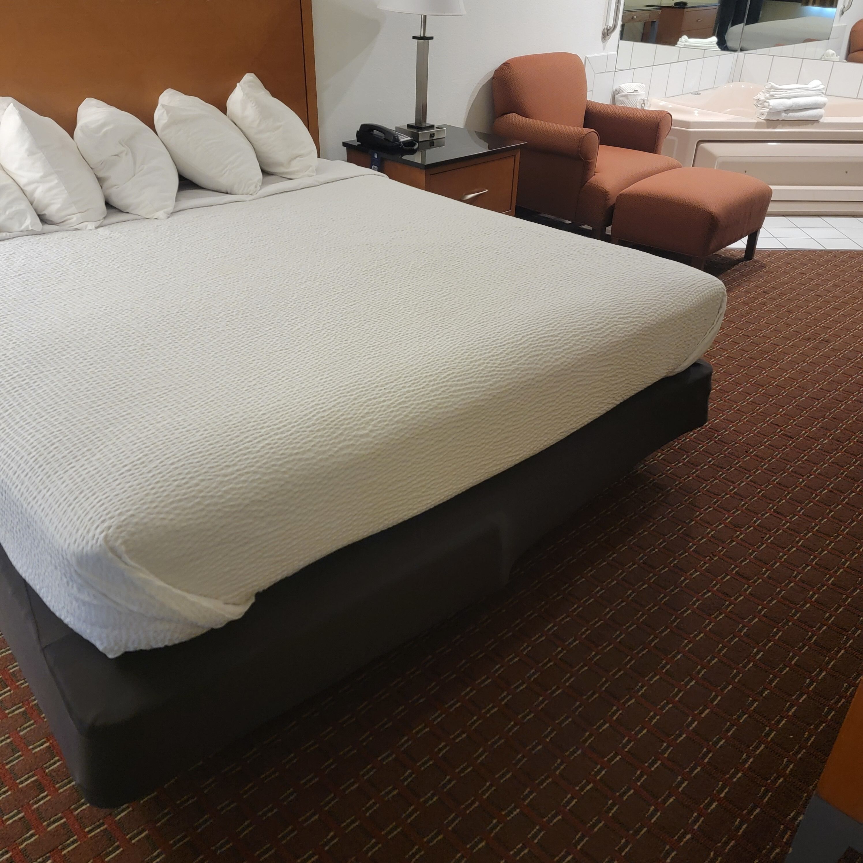 A hotel room with a large bed, a desk with a lamp, a chair, and a bathroom area.