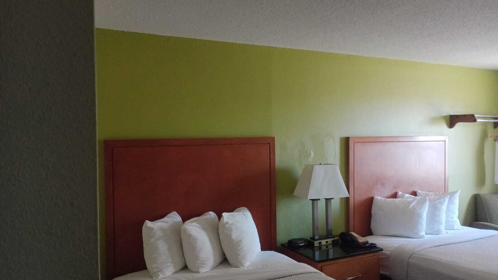 Een hotelkamer met twee bedden, elk met een houten hoofdbord, een nachtkastje met een lamp en een klein tafeltje.
