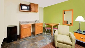 Une petite cuisine équipée d’un four à micro-ondes, d’un évier et d’un petit réfrigérateur. On y trouve une table à manger avec deux chaises et un canapé.