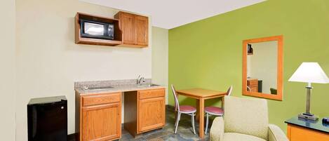 A compact kitchenette with a microwave, sink, and small refrigerator. There is a dining table with two chairs and a single sofa.