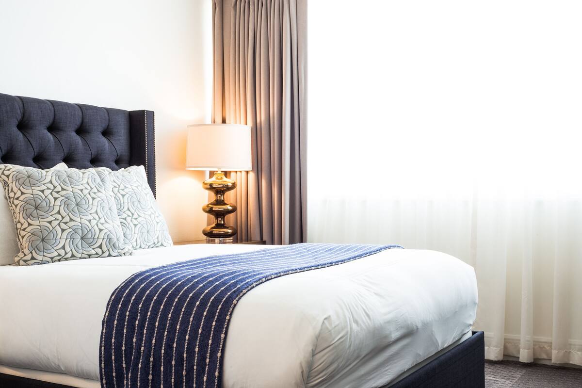 A neatly made bed with a dark headboard, a patterned pillow, a blue striped blanket, and a bedside lamp.