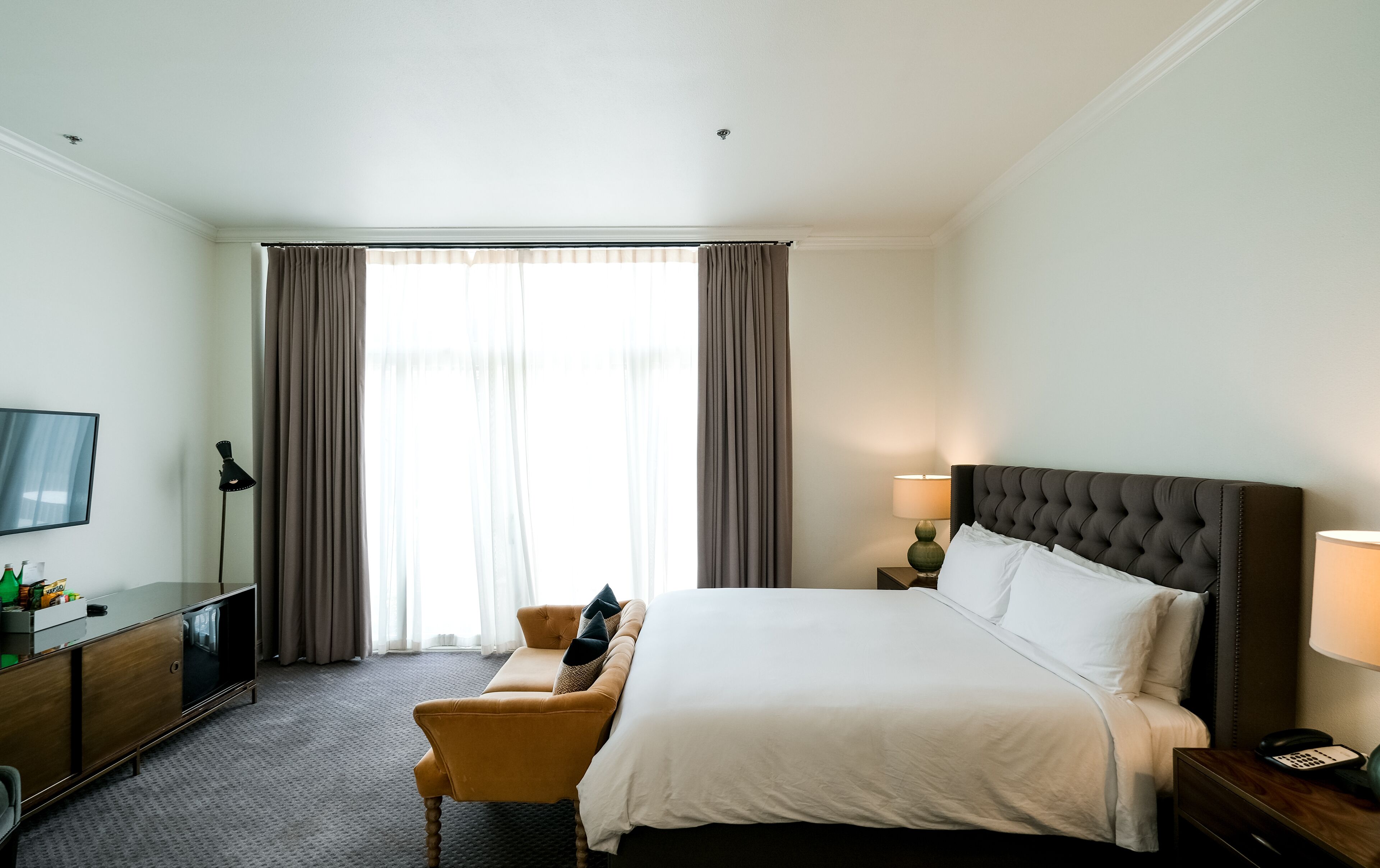 Habitación de hotel con cama, escritorio, silla, televisor y ventana con cortinas.