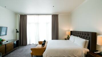 Habitación de hotel con cama, escritorio, silla, televisor y ventana con cortinas.