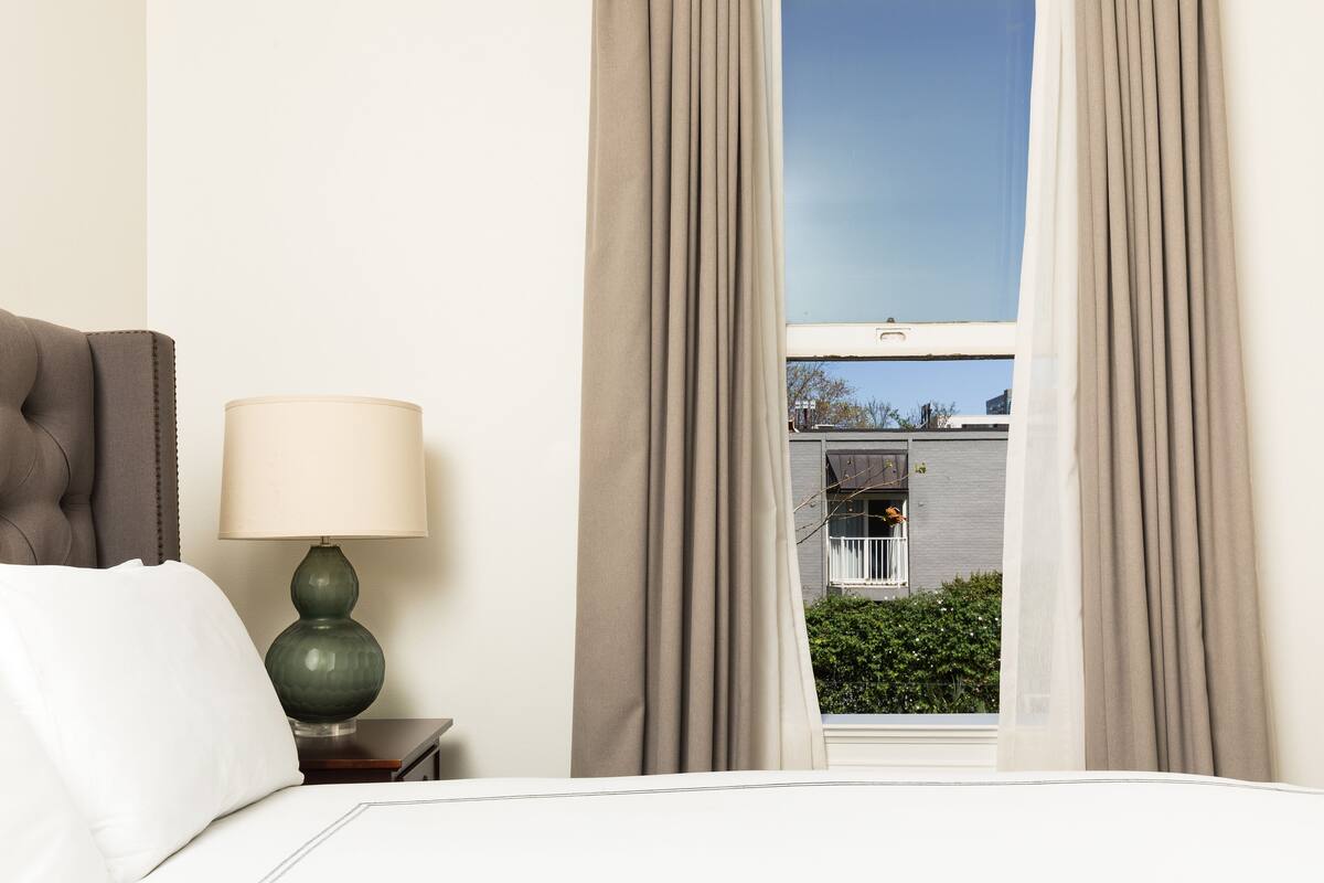 A hotel room with a bed, a green lamp, and a window with curtains.