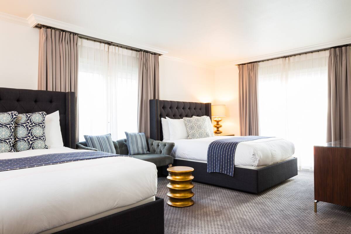 A hotel room with two beds, a sofa, a round gold side table, and a wooden nightstand.