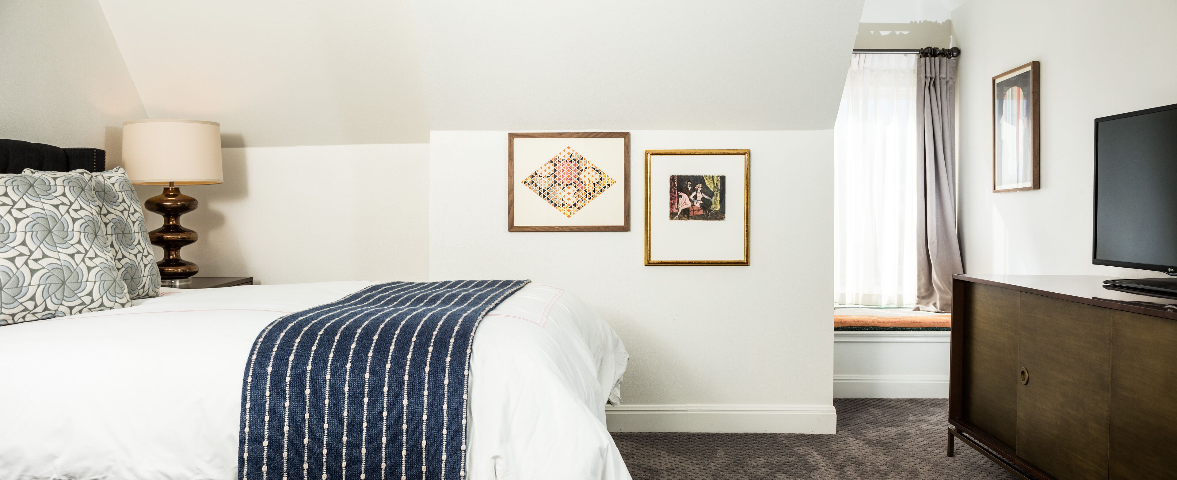 Una habitación de hotel con cama, lámpara, televisor y dos cuadros en la pared.