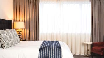 A hotel room with a bed, a bedside lamp, a red chair, and a small table with a tray of items.