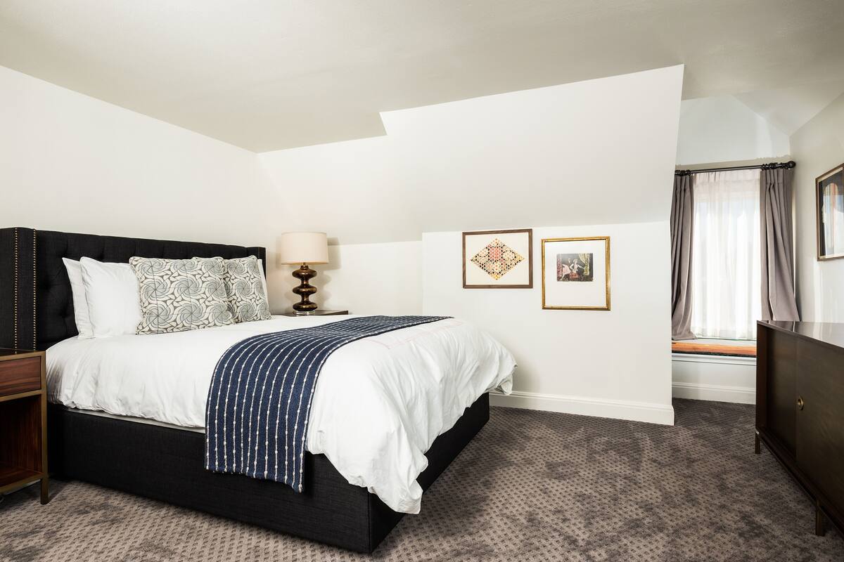 A bedroom with a large bed, a bedside table, a lamp, and two framed pictures on the wall.