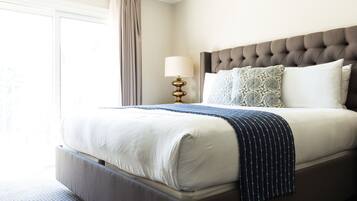 A neatly made bed with a headboard, a bedside lamp, and a window with curtains.