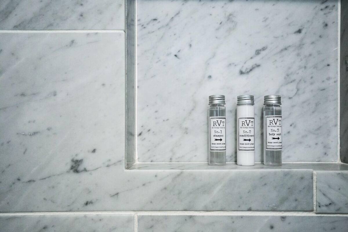Tres botellas de gel de baño RVT sobre un repisa con azulejos de mármol.