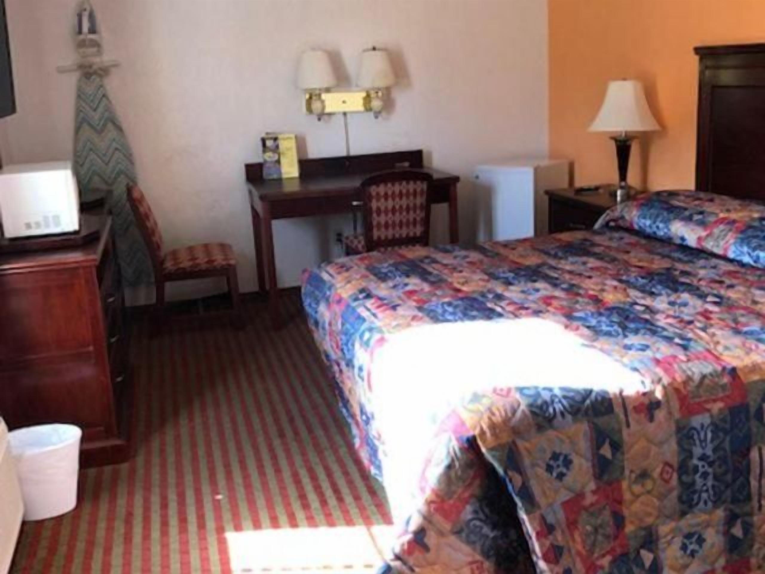 Een hotelkamer met een bed, bureau, stoel en een kleine tafel met een lamp.