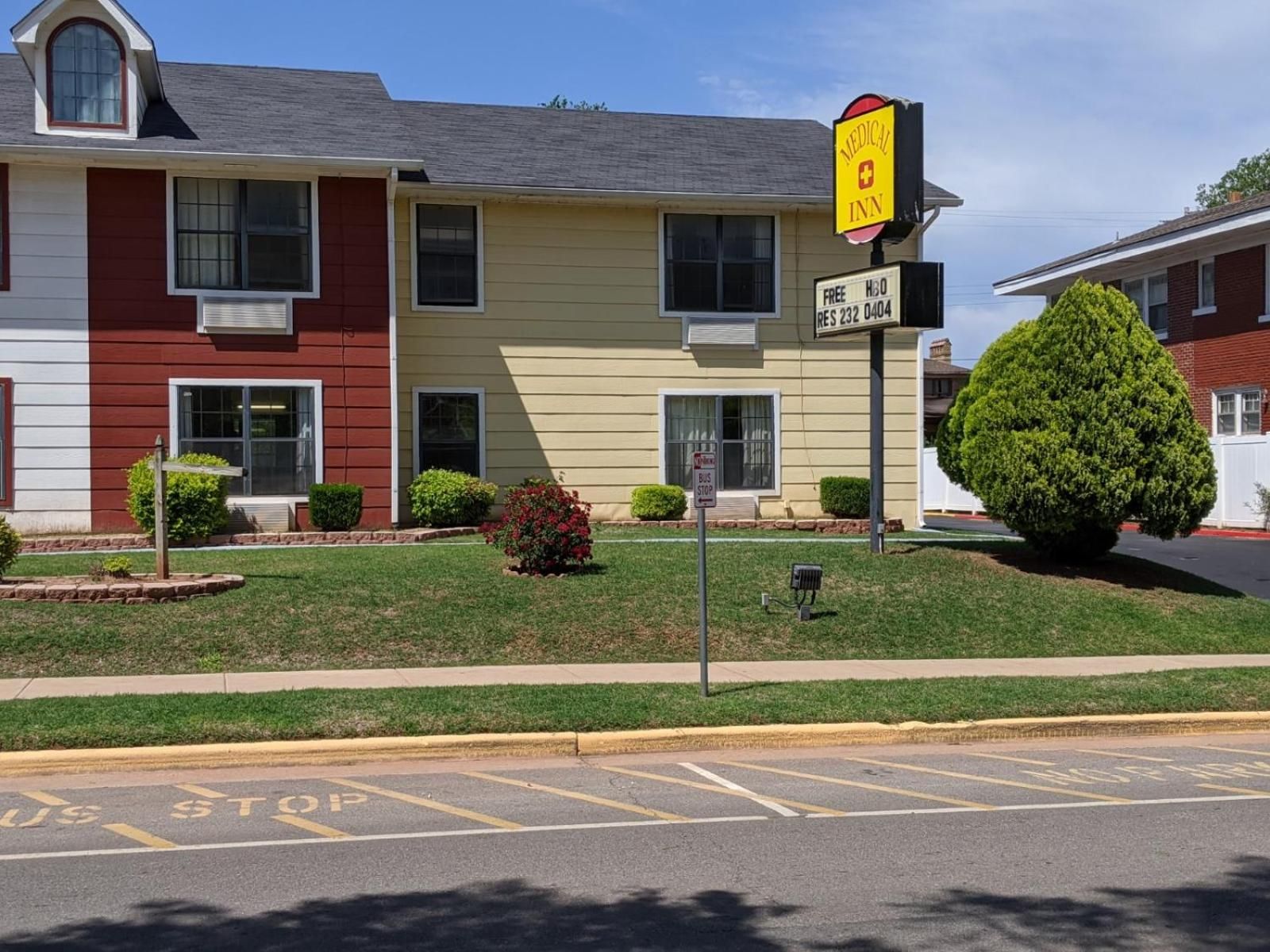 A two-story building with a medical facility sign, a bus stop sign, and a parking lot with marked spaces.