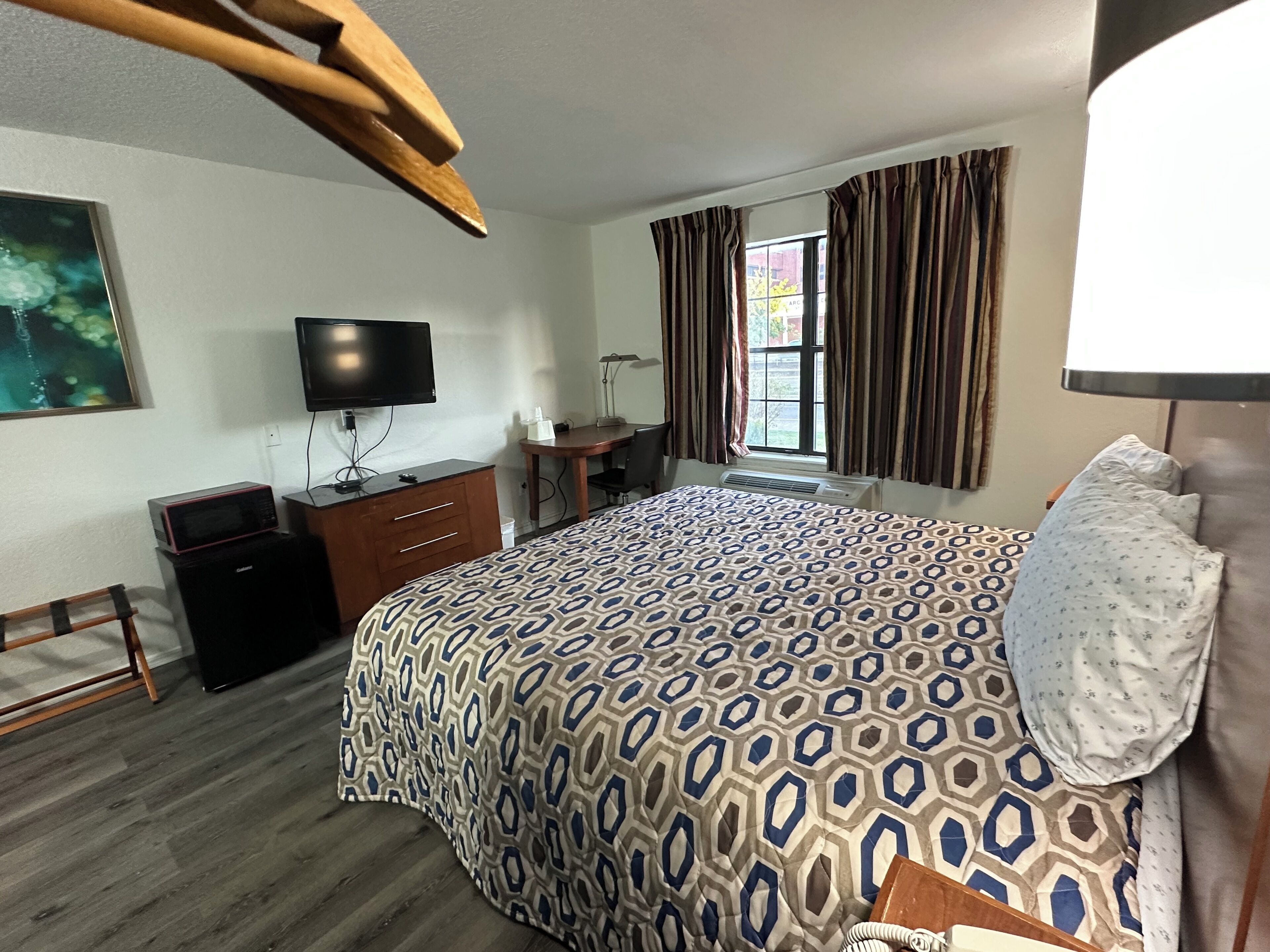 Une chambre d’hôtel avec un grand lit, un bureau, une télévision, un four à micro-ondes et une fenêtre avec des rideaux.