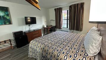 Une chambre d’hôtel avec un grand lit, un bureau, une télévision, un four à micro-ondes et une fenêtre avec des rideaux.