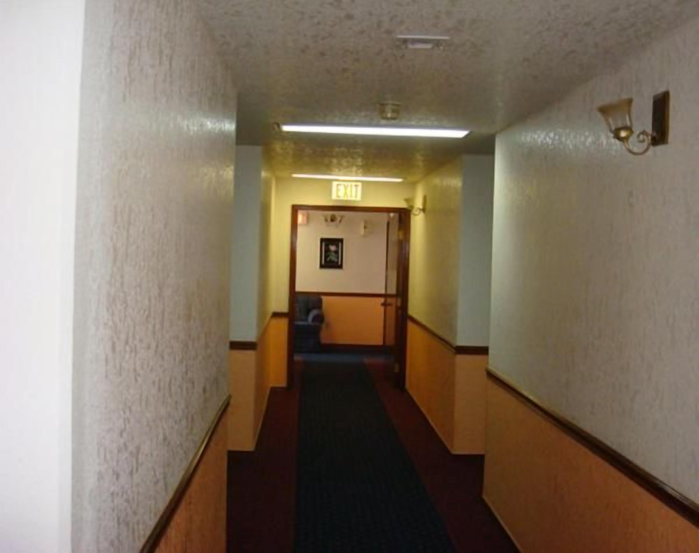 A narrow hallway with a carpeted floor, wooden walls, and a door at the end.