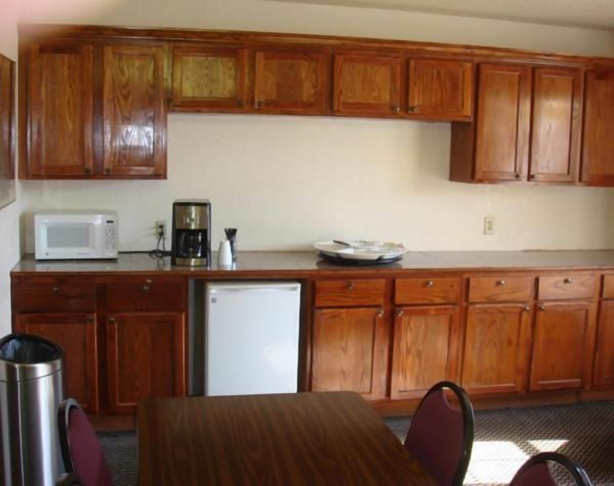 A compact kitchen with wooden cabinets, a microwave, a coffee maker, and a refrigerator.