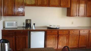 A compact kitchen with wooden cabinets, a microwave, a coffee maker, and a refrigerator.
