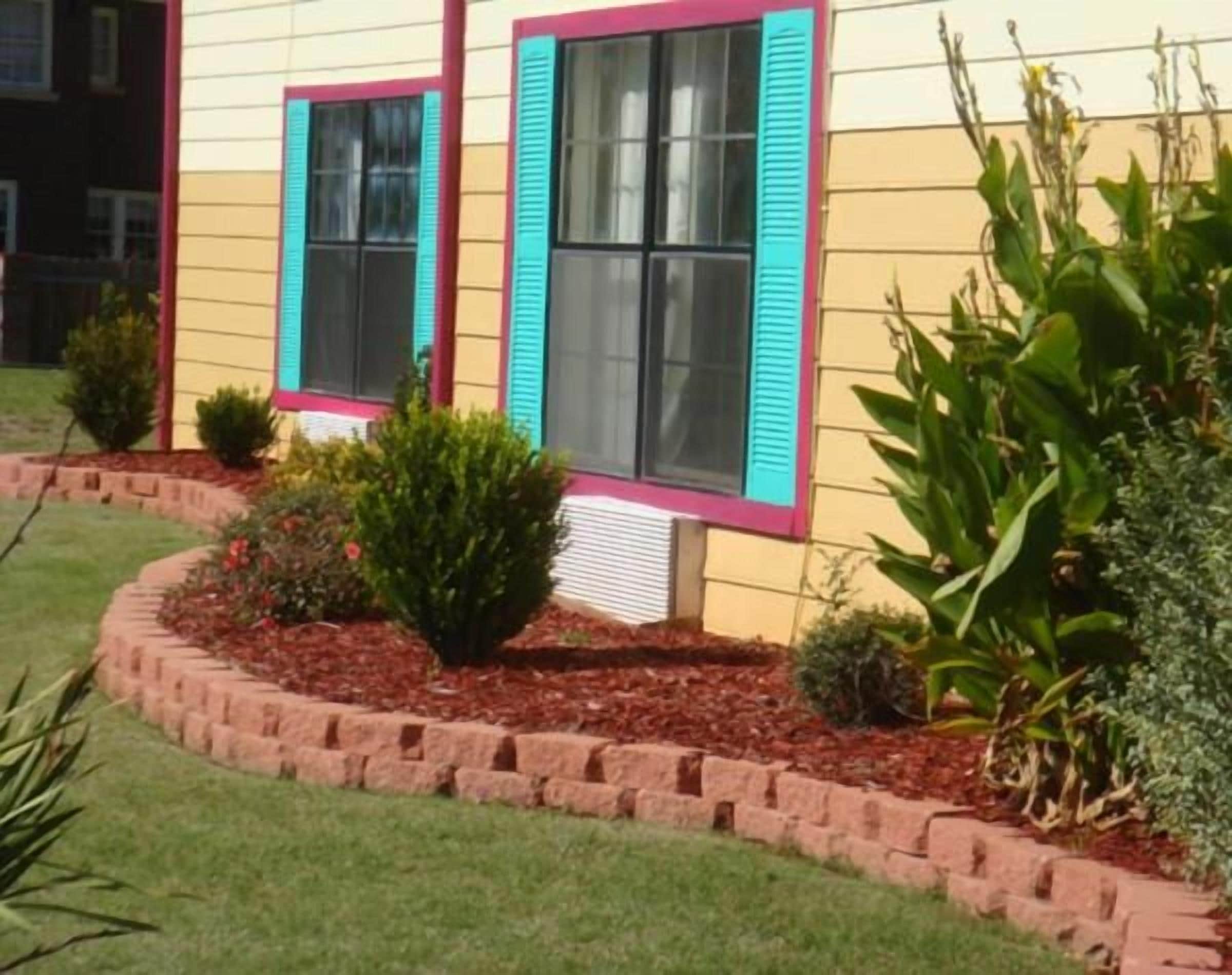A house with a front yard, a brick border, and a window with shutters.