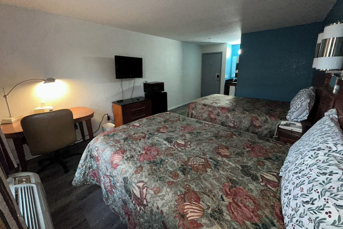 A hotel room with two beds, a desk, a chair, a TV, and a lamp.