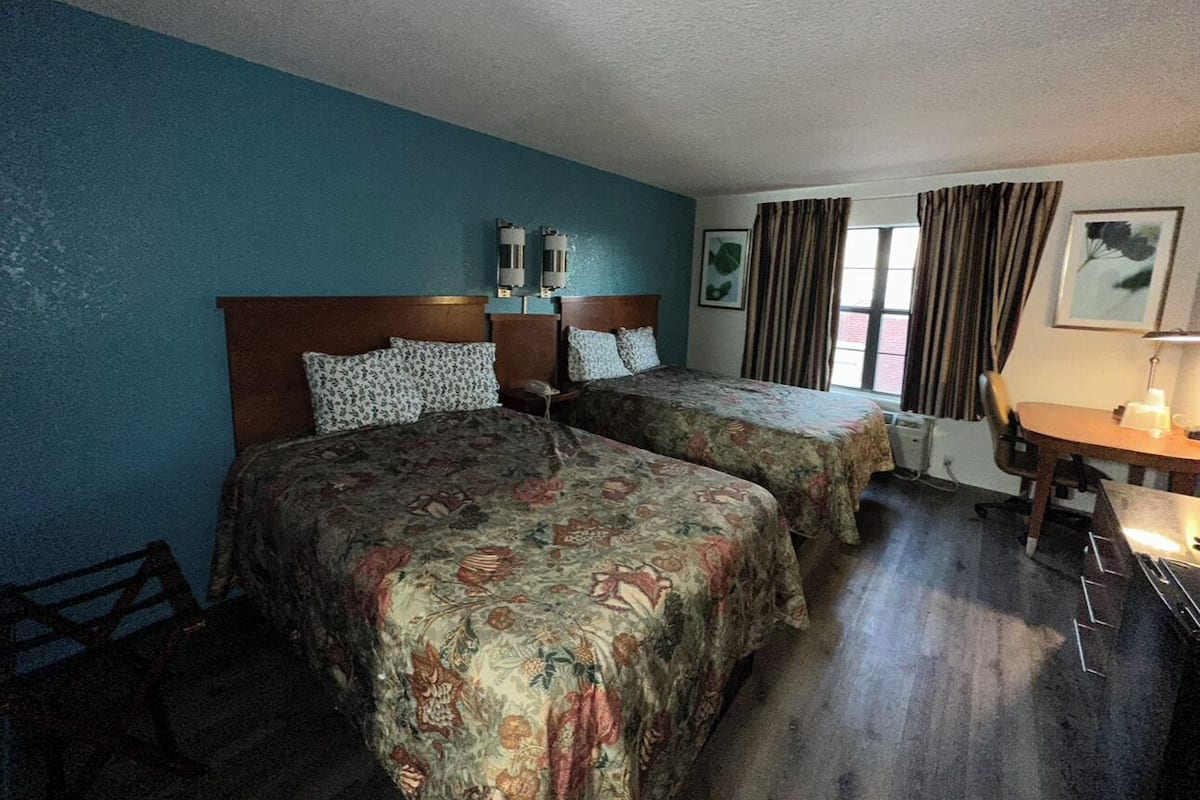 A hotel room with two beds, a desk, and a window with curtains.