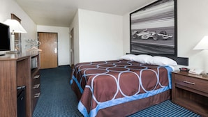 A hotel room with a bed, a desk with a lamp, a television, and a large framed picture on the wall. - Super 8 by Wyndham Greenfield (Greenfield)