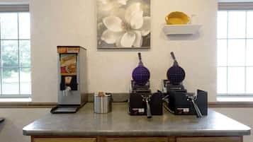 A kitchen counter with a waffle maker, a coffee machine, and a box of cereal.