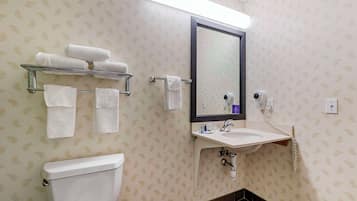A bathroom with a toilet, a sink with a mirror, and a towel rack with several towels.