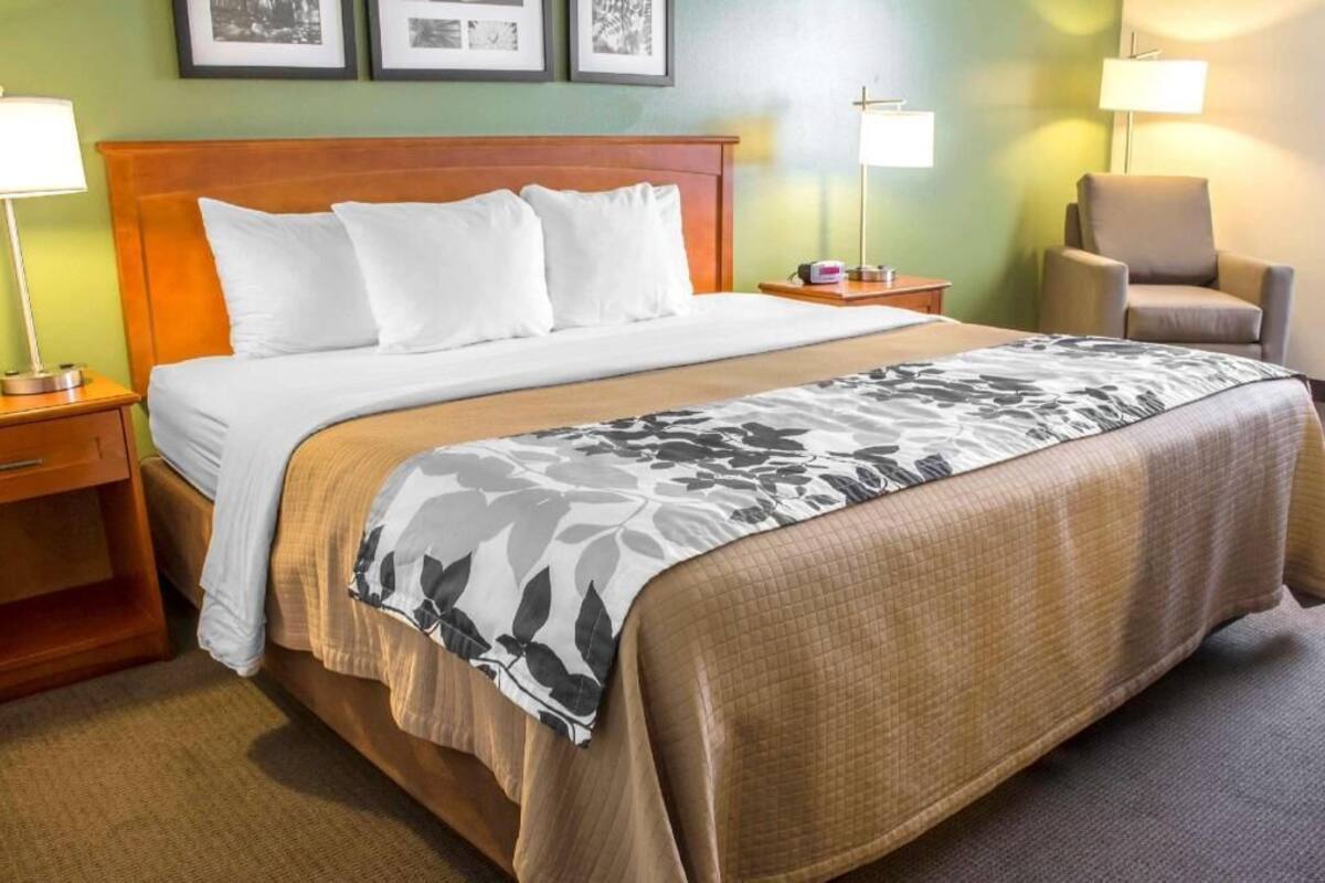 A hotel room with a bed, bedside tables, a chair, and framed pictures on the wall.