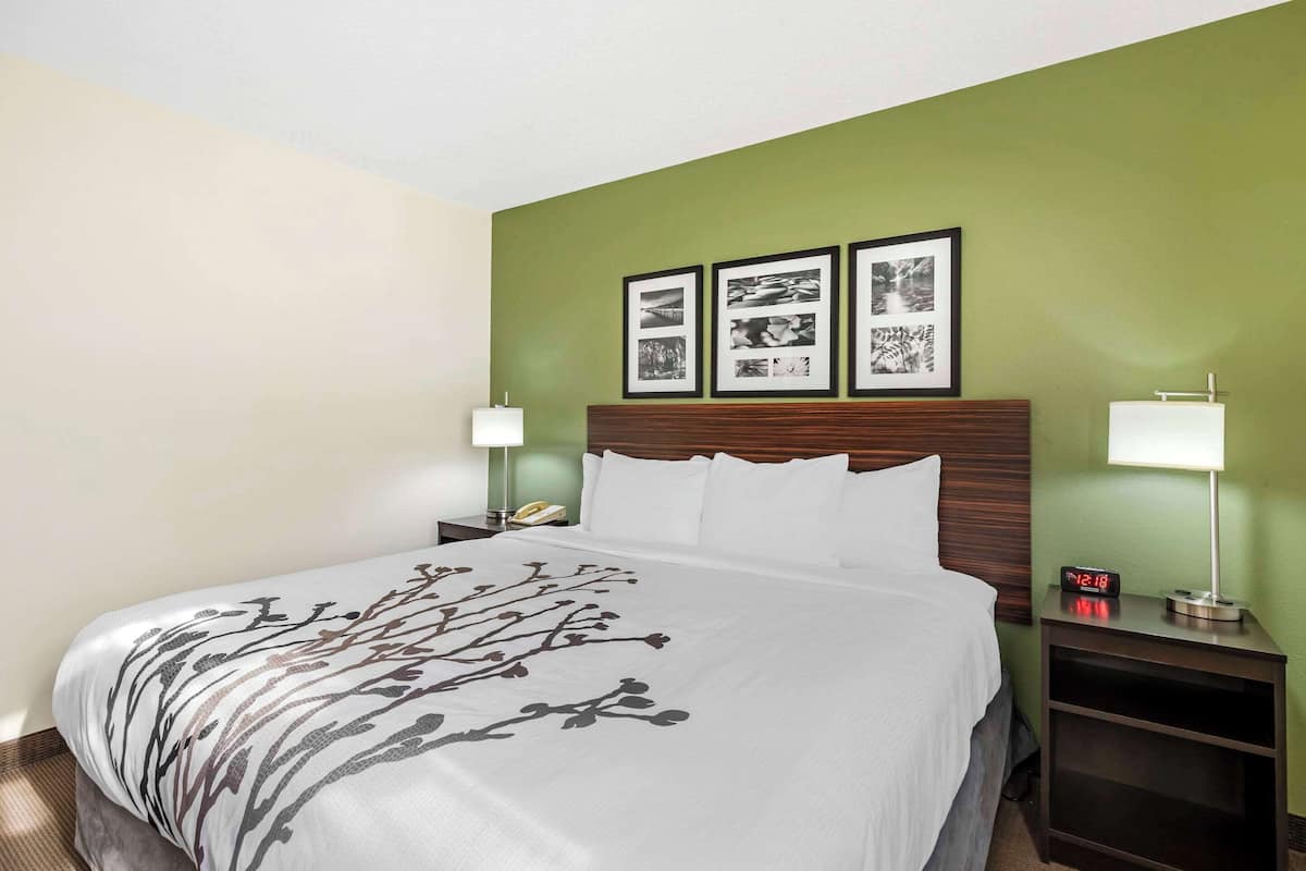 A hotel room with a bed, two bedside tables, a nightstand, and three framed pictures on the wall.