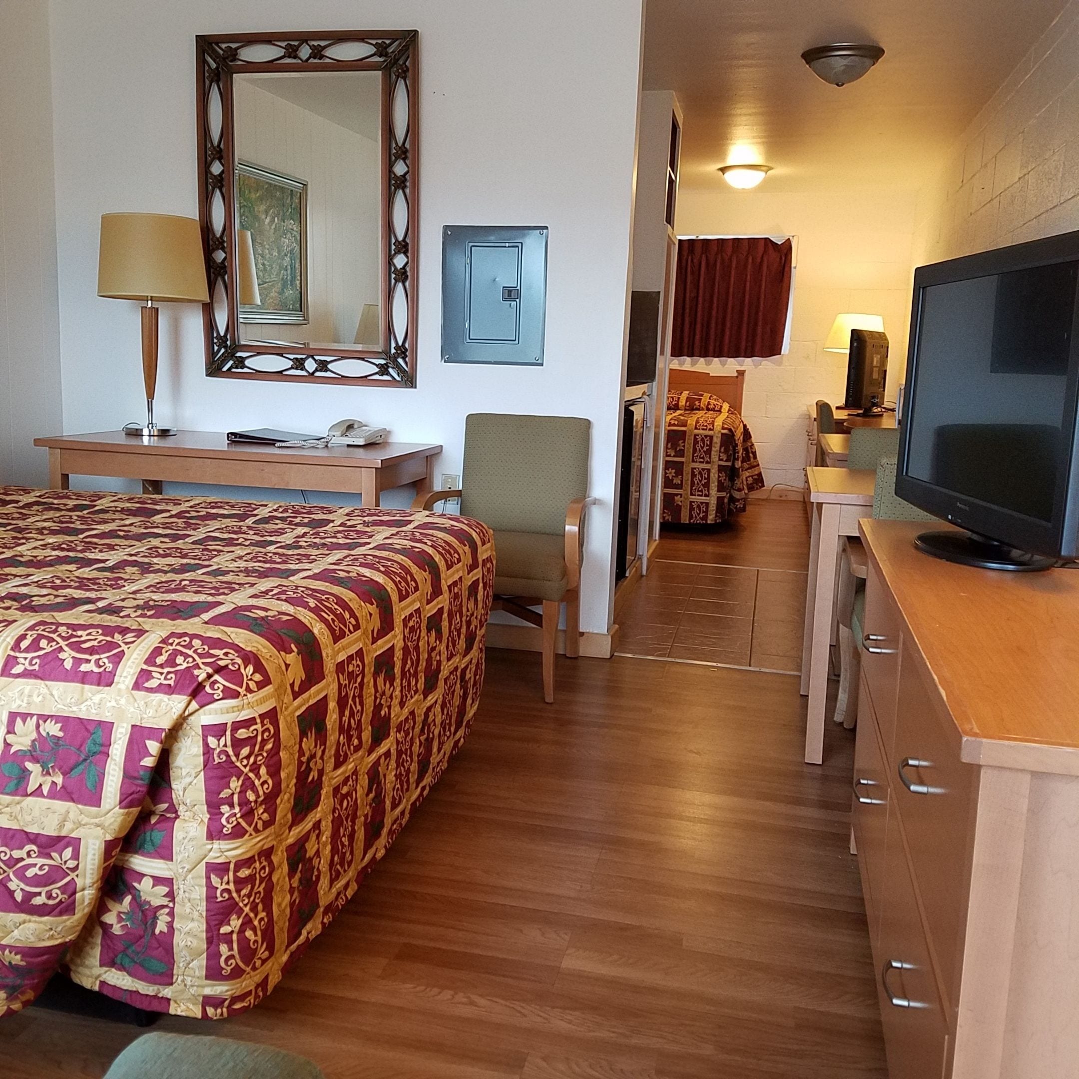 A hotel room with a bed, a desk, a chair, a television, and a mirror.