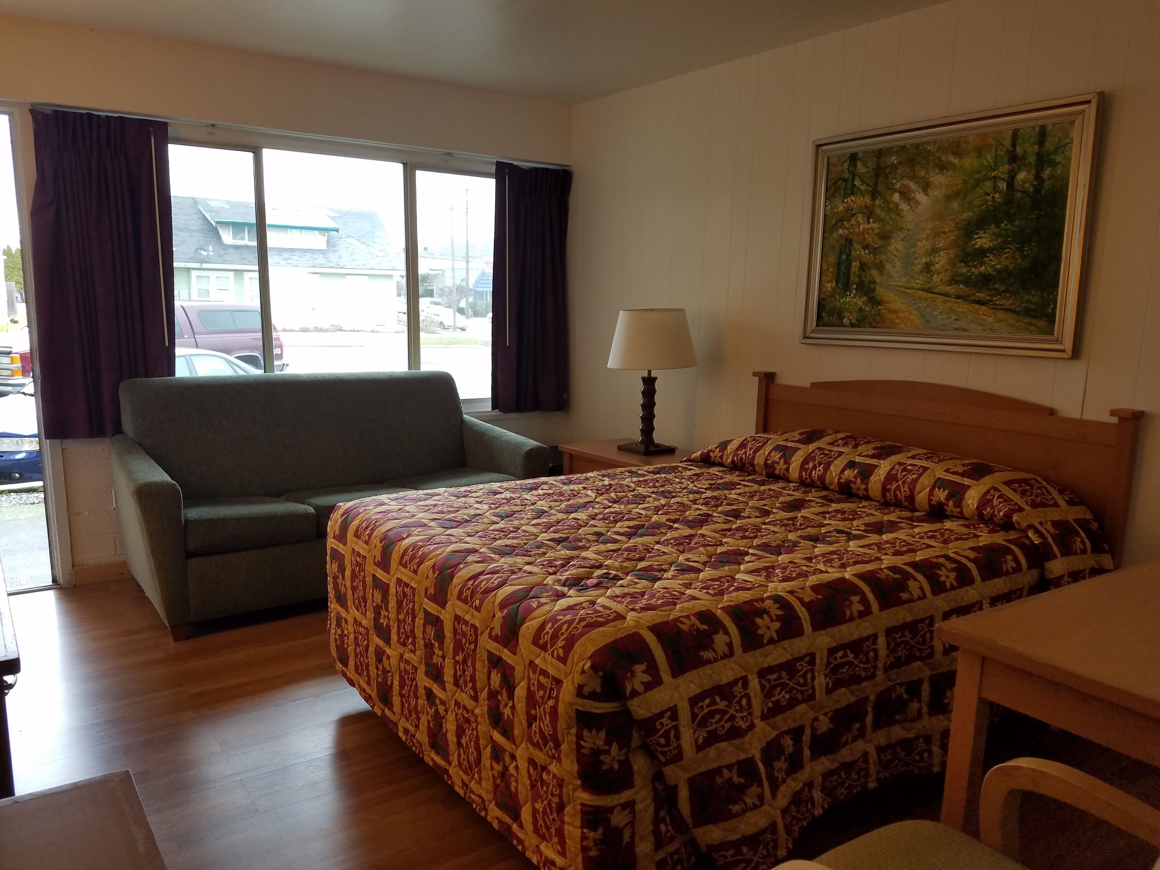 Una camera d'albergo con un letto, un divano, un tavolo, una lampada e un quadro appeso al muro.