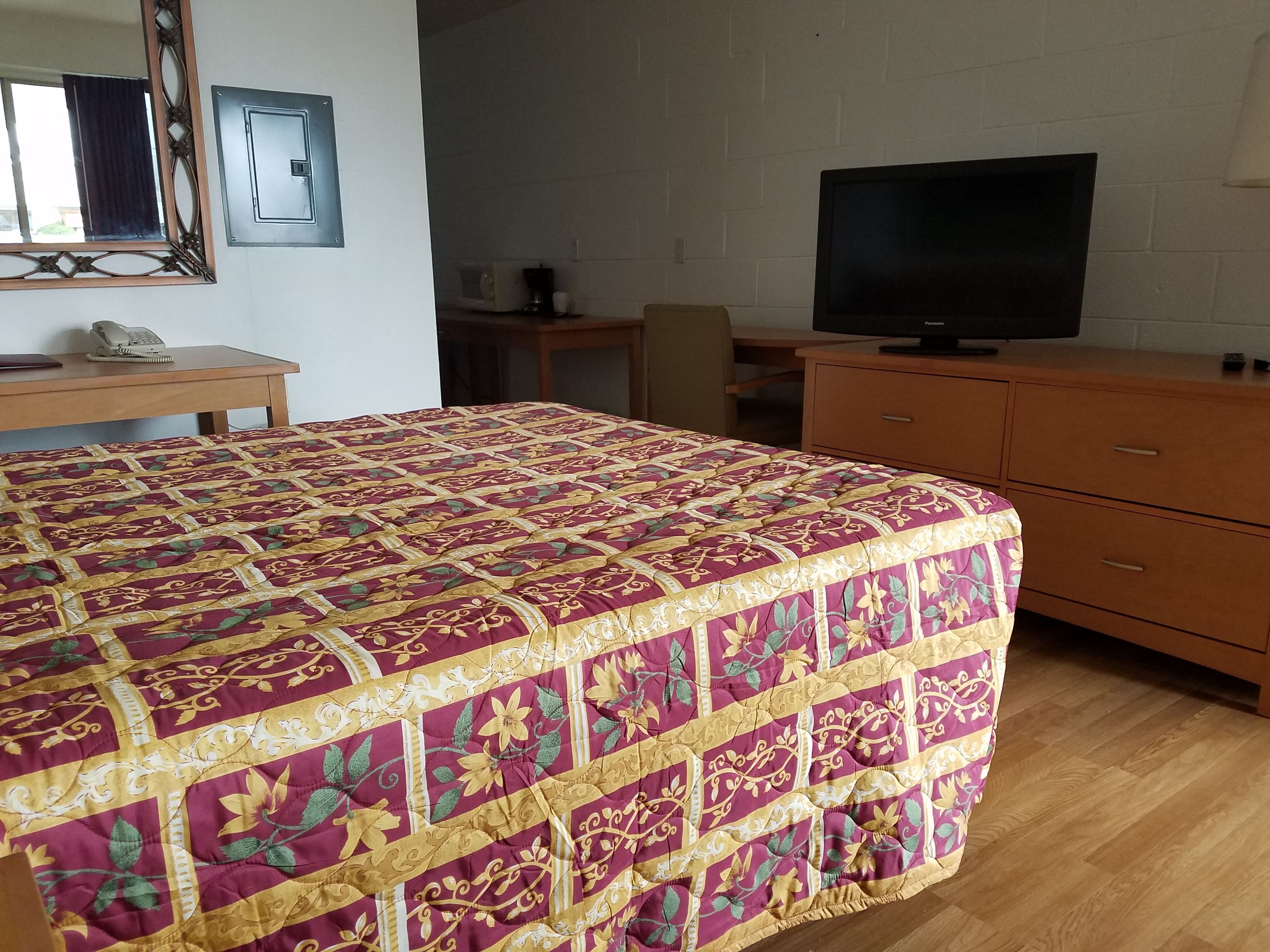 A bedroom with a large bed, a wooden dresser, a television, and a desk with a chair.