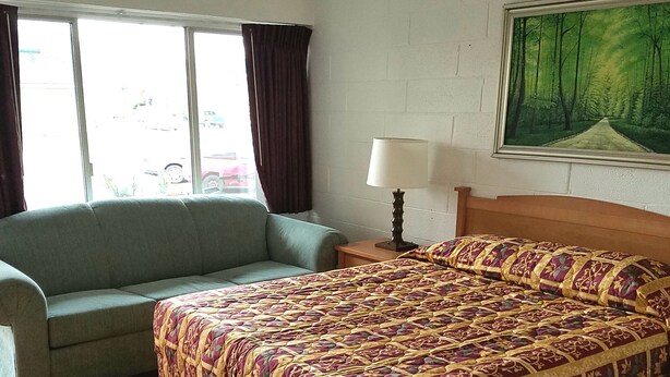 A room with a bed, a sofa, a window with curtains, a lamp, and a painting on the wall. - San Juan Motel (Anacortes)
