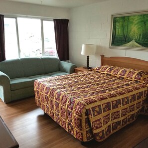 A room with a bed, a sofa, a window with curtains, a lamp, and a painting on the wall. - San Juan Motel (Anacortes)