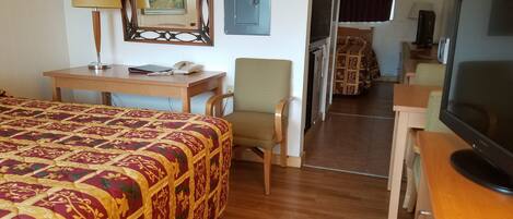 A hotel room with a large bed, a desk with a telephone, a chair, a television, and a mirror.