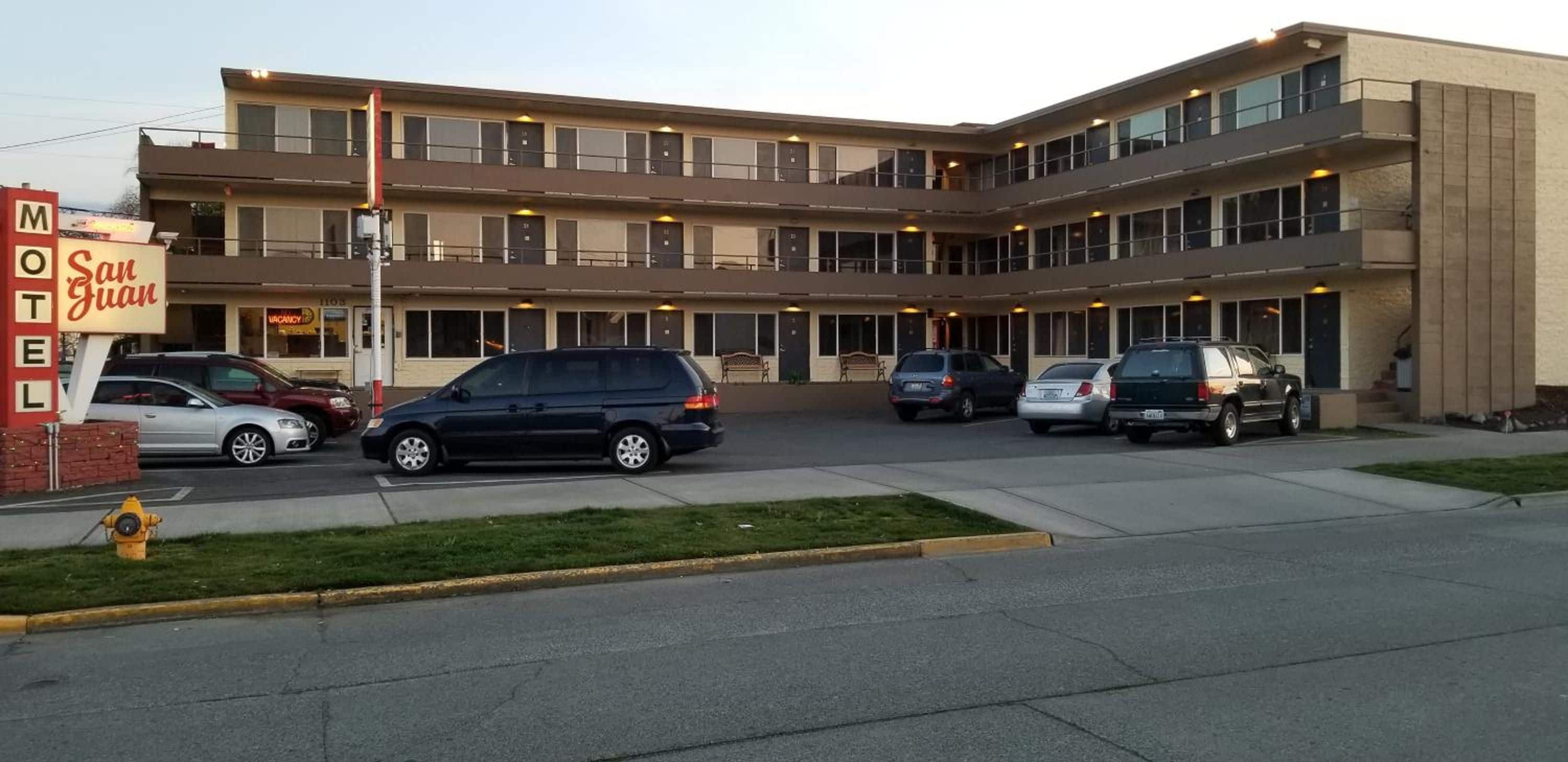 Un motel con varios pisos, un estacionamiento y varios autos estacionados al frente.