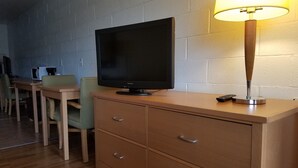 A room with a television on a wooden cabinet, a lamp on a table, and a chair. - San Juan Motel (Anacortes)