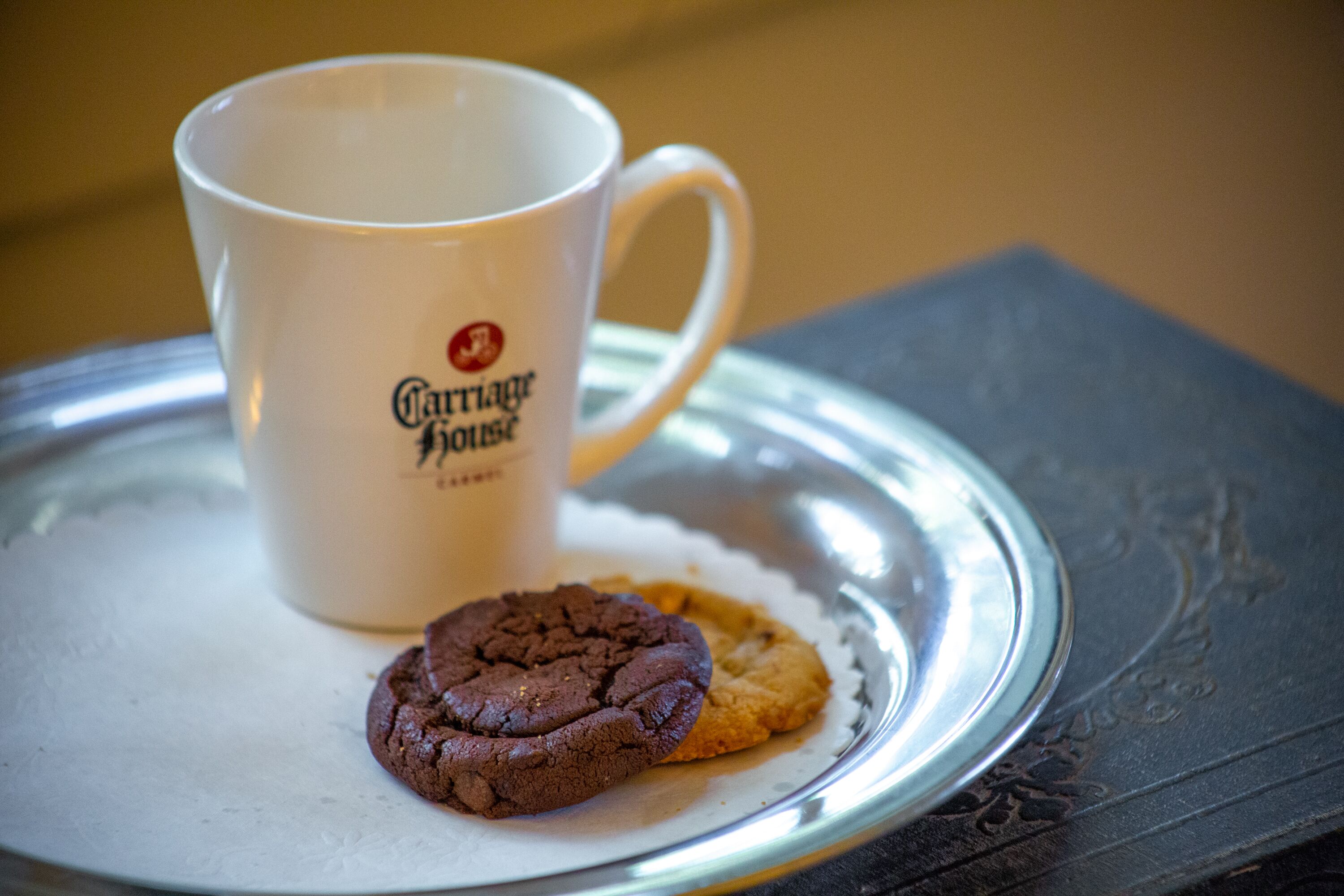 A white mug with a logo and two cookies on a silver tray.