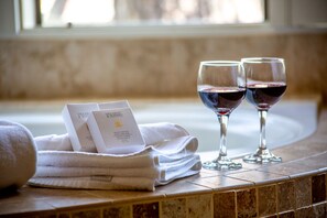 A bathroom with two glasses of red wine, a stack of white towels, and a bottle of Gilchrist & Soames bath and shower gel.