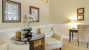 Una habitación con una mesa redonda, dos sillas, un florero con flores y cuadros en la pared.