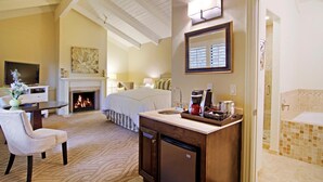 Habitación de hotel con chimenea, cama, escritorio con televisor, estación de café y baño con bañera.