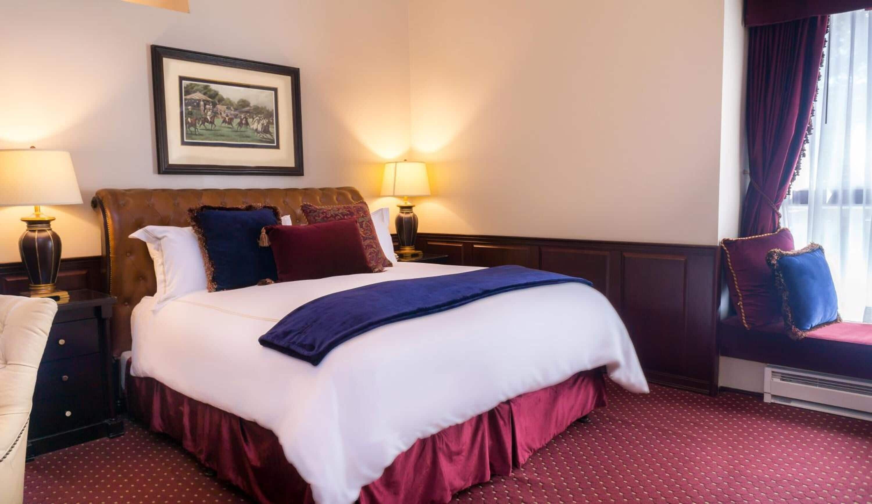 A hotel room with a large bed, two bedside tables with lamps, a framed picture on the wall, and a window with curtains.